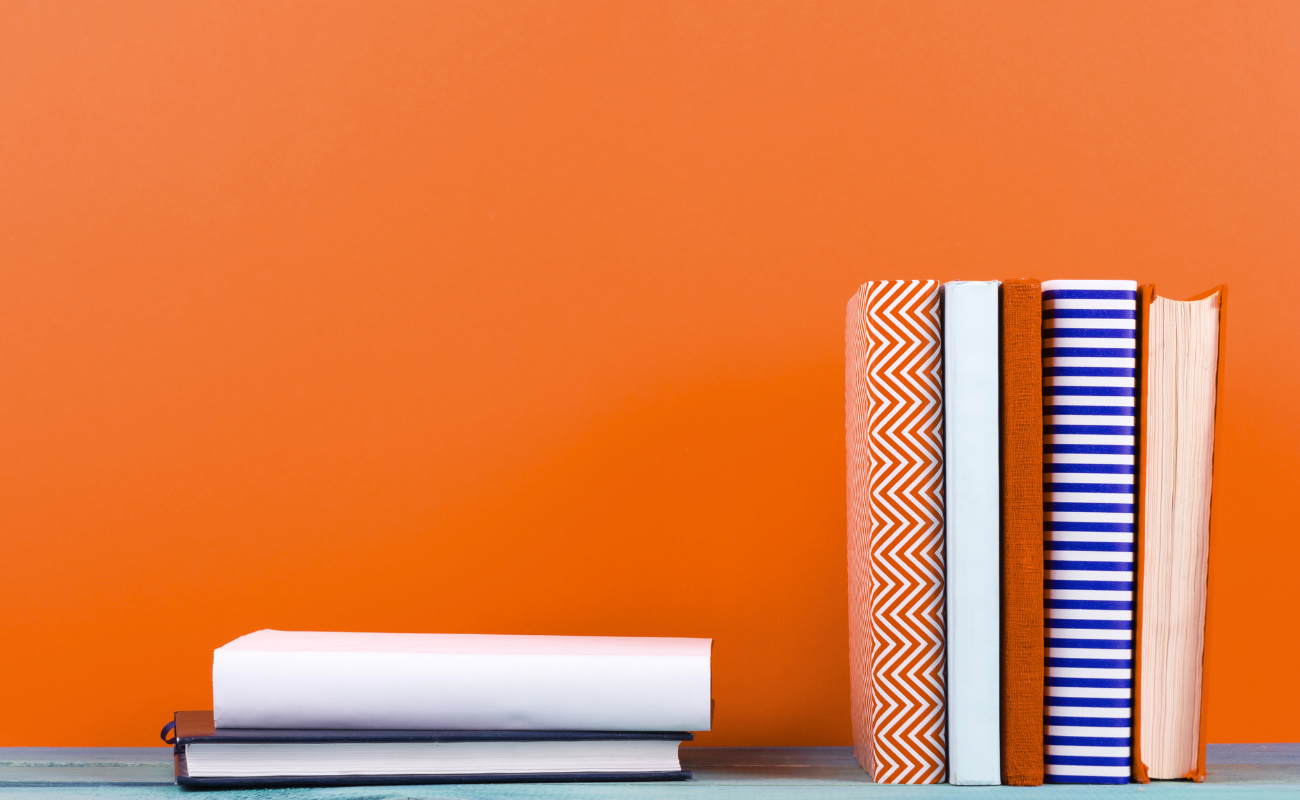 Strategic brand positioning and messaging services that define identity and drive engagement. Stack of colorful books on an orange surface, symbolizing brand standards and guidelines that ensure consistency in messaging and visuals as brands grow.