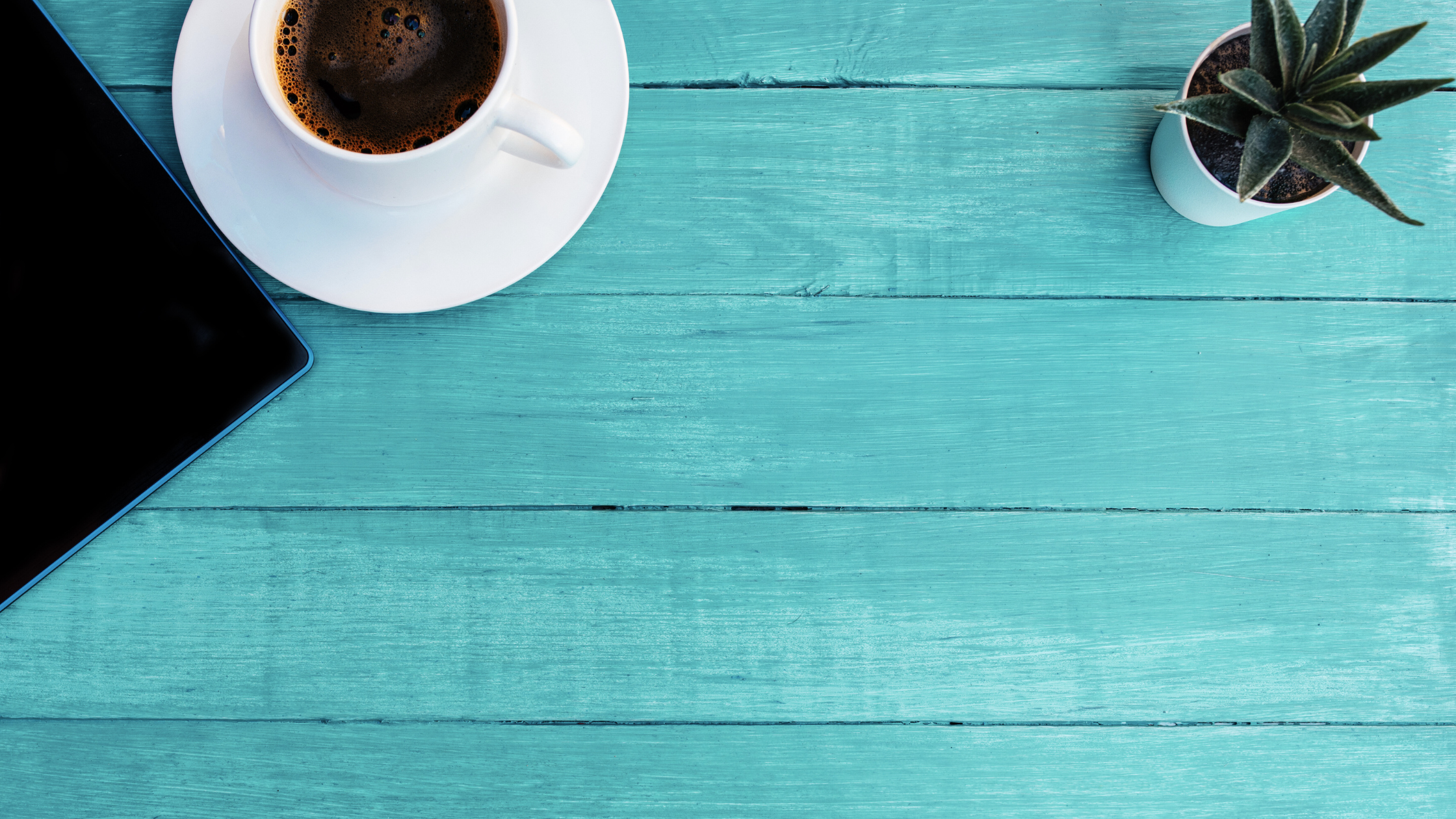 magtyne blog image_what a full-stack marketing partner actually does Top-down view of a workspace with a coffee cup, smartphone, and small plant on a turquoise wooden table.
