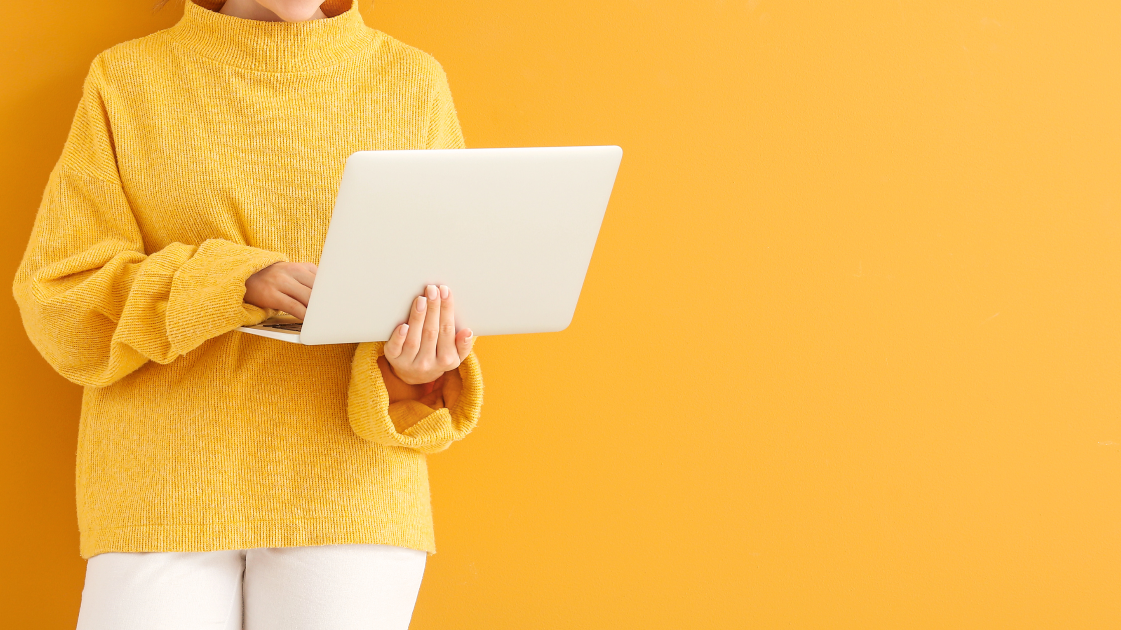 magtyne_blog image_teach market to see value Person in a yellow sweater holding an open laptop while working against a yellow background.